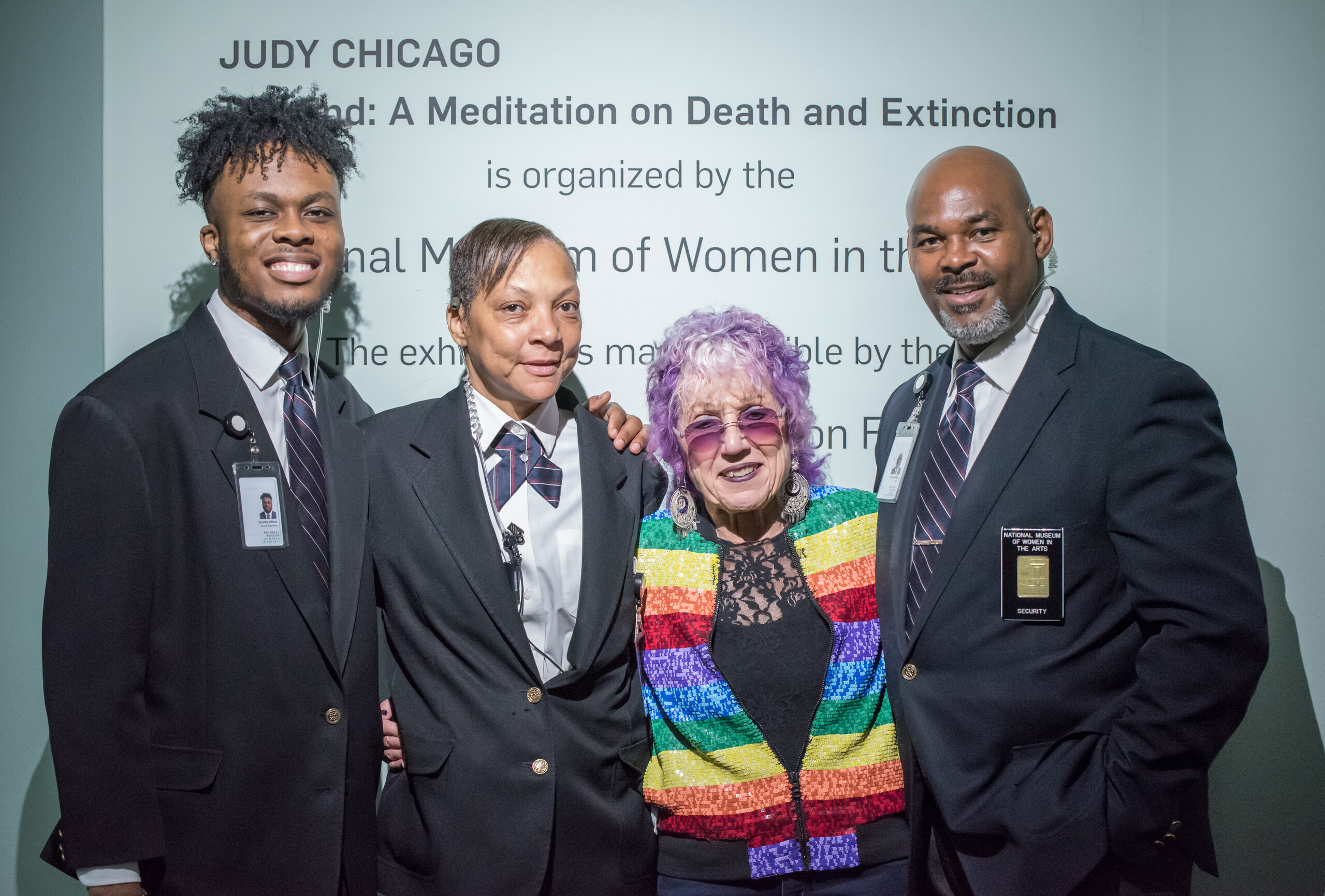 Three Security Officers and artist Judy Chicago stand next to each other smiling in front of opening text to the artist's exhibition.