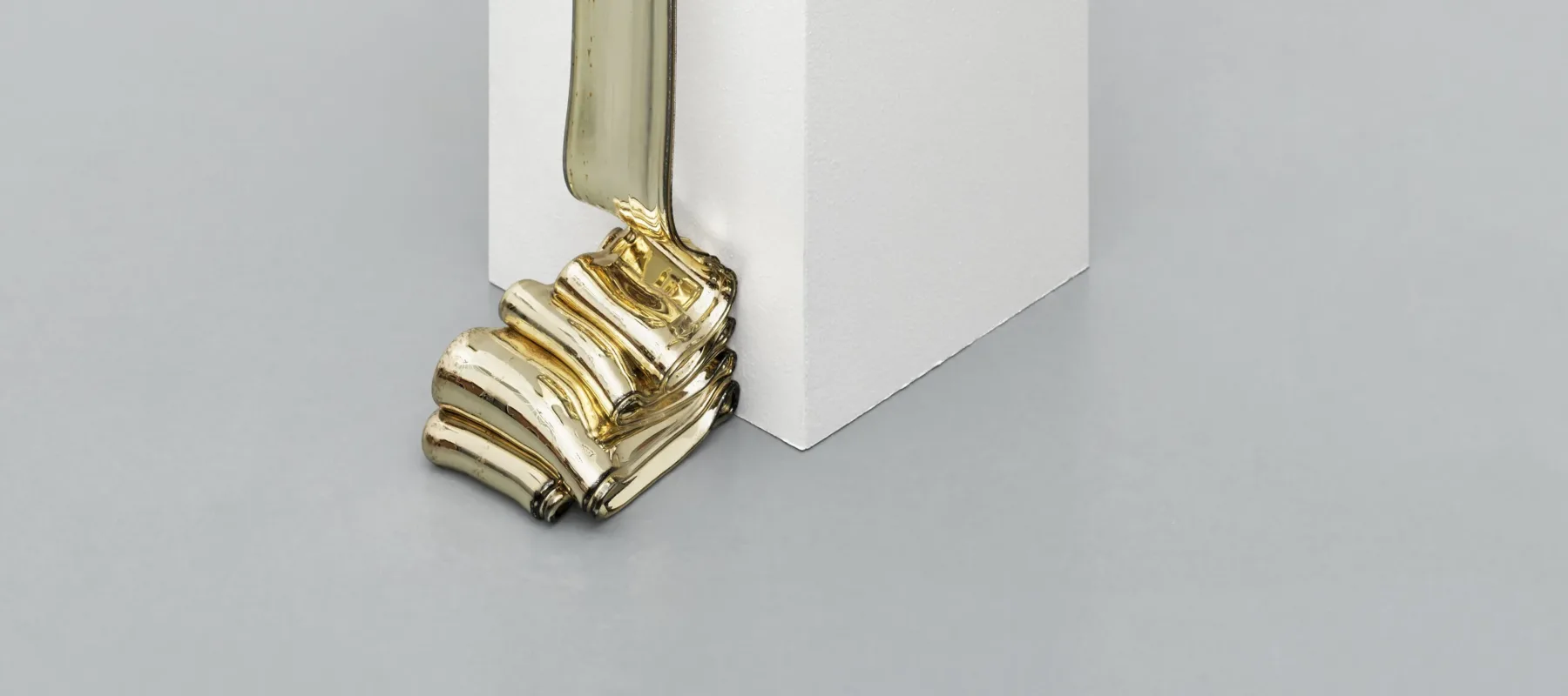 A solidified melted silver mass that sits on a white platform and cascades over one edge and ripples onto the floor.