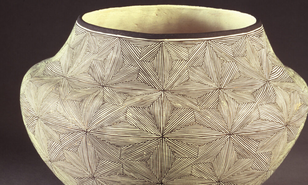 Ceramic jar, featuring a short neck and broad shoulders tapering to a narrow base, is decorated in a geometric, black and white quilt-like pattern. The matte, off-white surface is adorned with  geometric, flower-like patterns created by very thin, precisely-placed black lines.