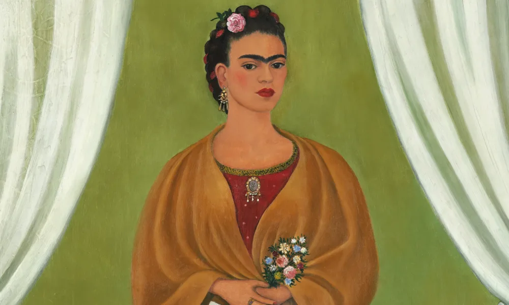 In a painted self-portrait, the artist stands in a stage-like space framed by white curtains. Beneath black hair woven with red yarn and flowers, heavy brows accent her dark-eyed gaze. Clad in a fringed, honey-toned shawl; long, pink skirt; and gold jewelry, she holds a bouquet and a handwritten letter.