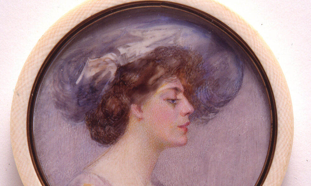 A miniature portrait in a round white frame of a light skinned woman in profile with brown hair pulled back in a loose bun. The woman wears a large periwinkle hat that matches the sleeves of her purple and blue dress. The background of the portrait is pale purple.