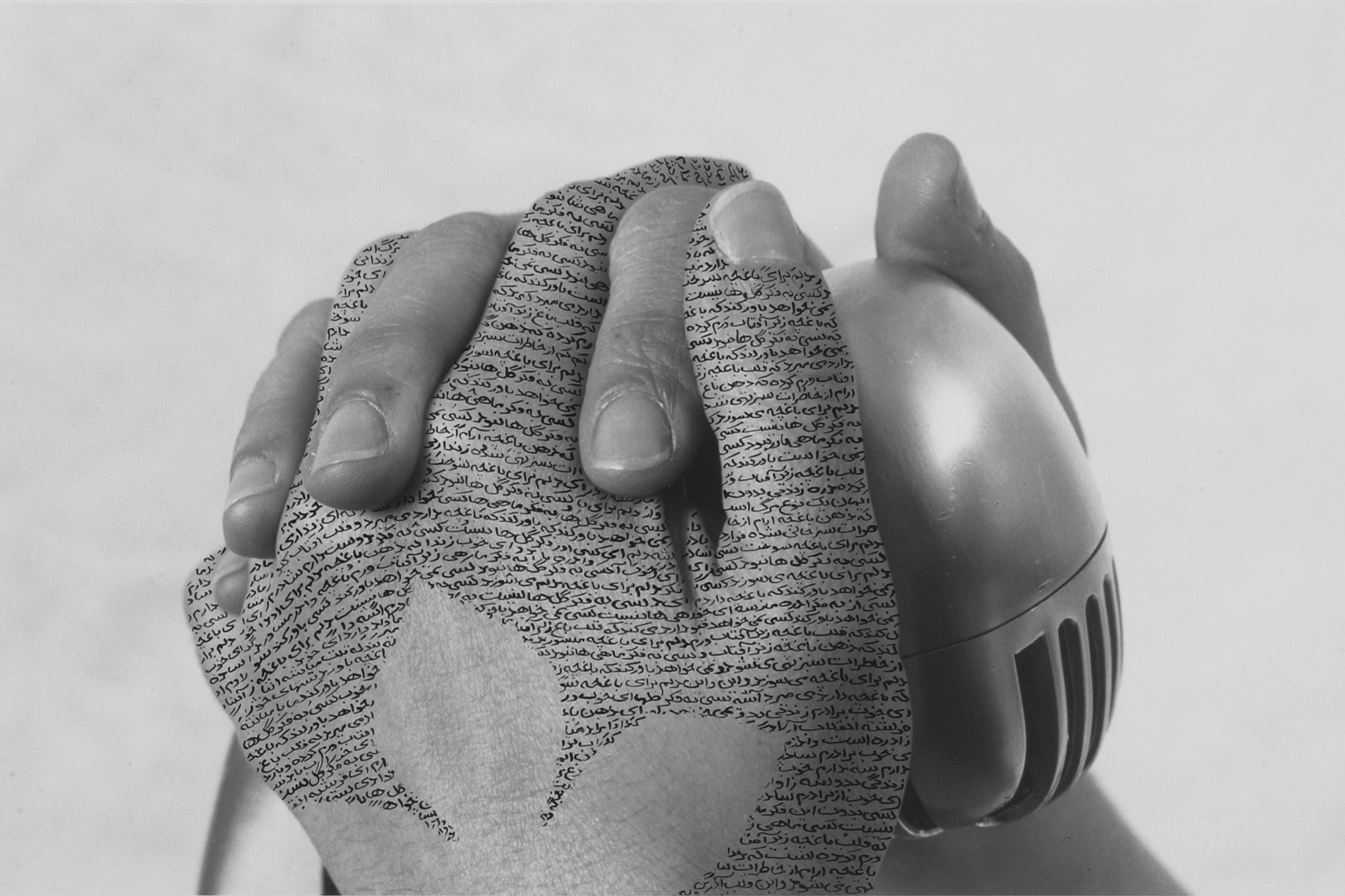 Close-up, black-and-white photograph of a woman's hands with fingers interlaced around a silver, vintage microphone. Lines of poetry inscribed in Farsi form a three-leaf shape on her left hand.