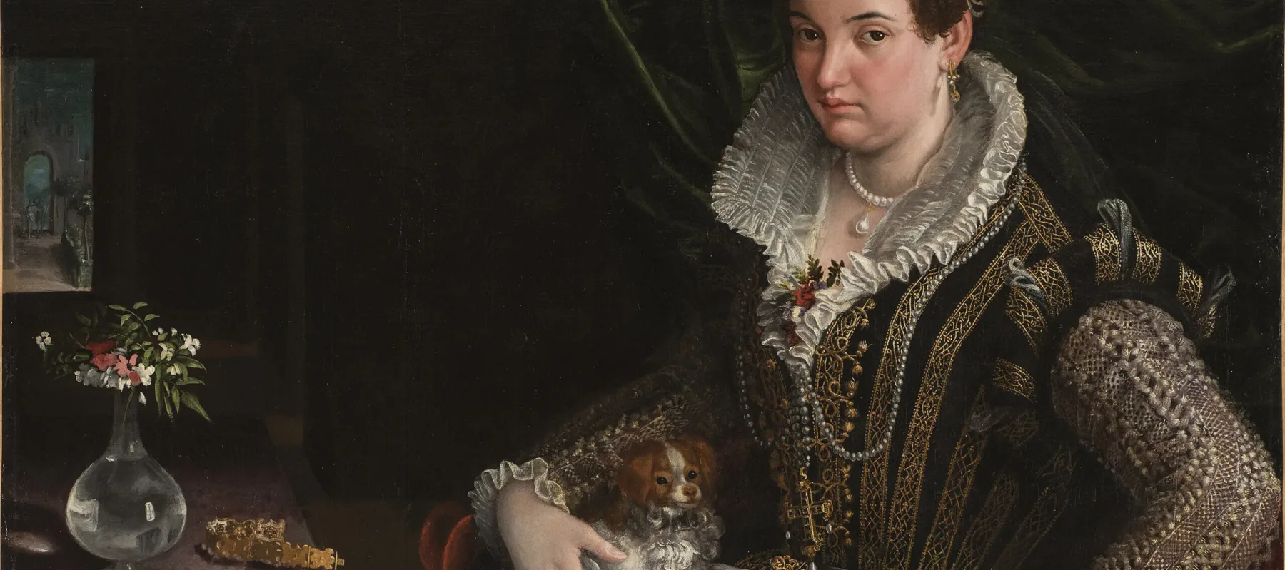 A light-skinned, dark-haired woman wearing pearl and gold jewelry and a black-velvet, lace, and brocade gown poses with her lap dog. Seated in a red velvet chair in the foreground, she makes eye contact with viewers while pressing her hand on the armrest, as if to stand.