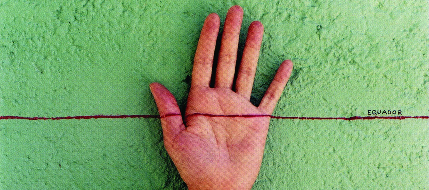 A light-skinned, left hand facing palm-out against a mottled, green-gray wall. A horizontal red line is drawn across the middle of the composition and the middle of the hand. On top of the red line on the right, is the word ‘EQUADOR’ written in small, black, capital letters.