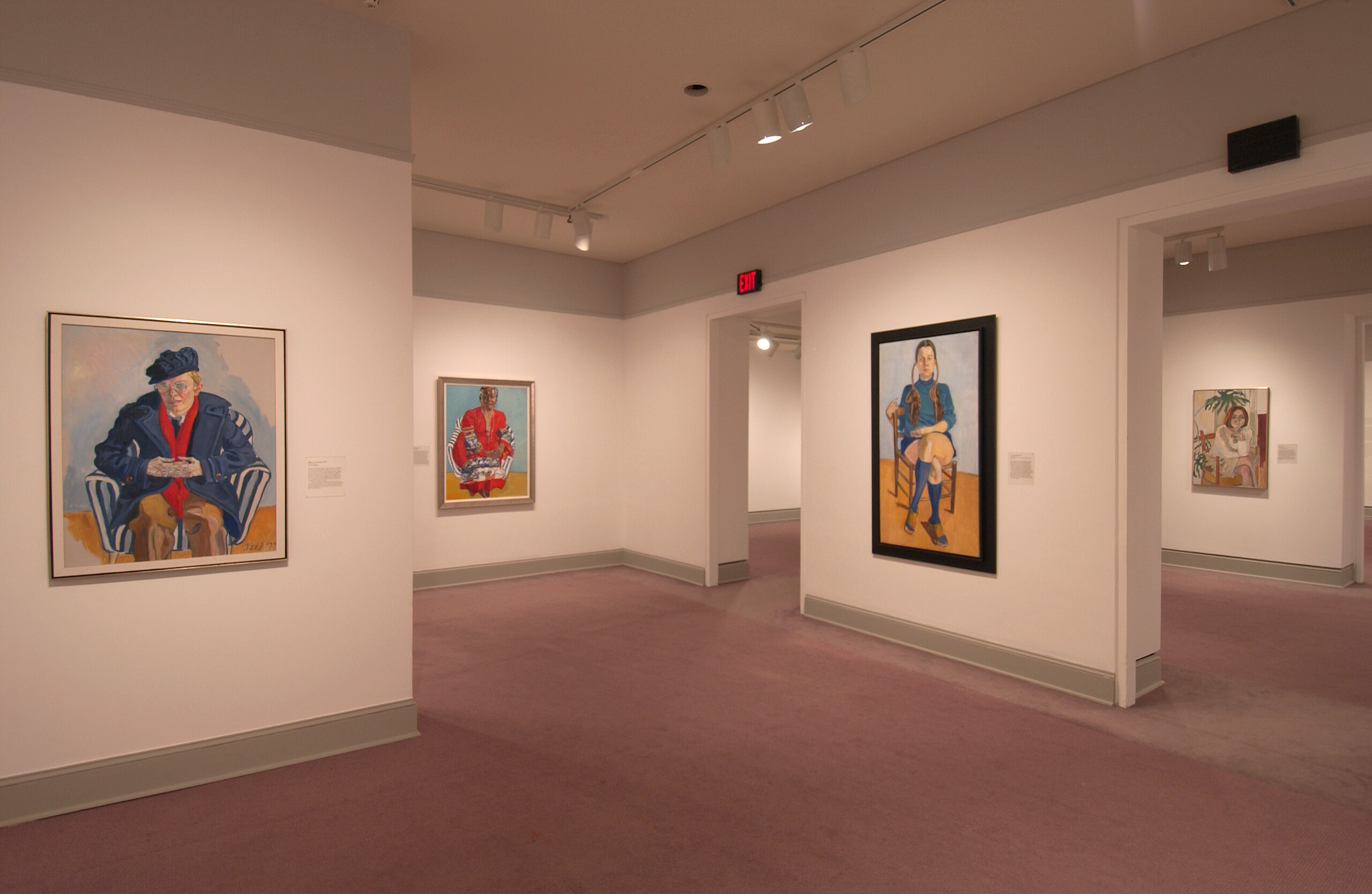An installation view of a gallery space shows several paintings hanging on a white wall. The paintings are colorful and show different women sitting in a chair. The woman portrayed on the left has a light skin tone and wears a blue coat and a blue beret, the woman in the painting in the center of the photograph has a medium-dark skin tone and wears a red dress, and the woman on the right painting has a light skin tone and pigtails.