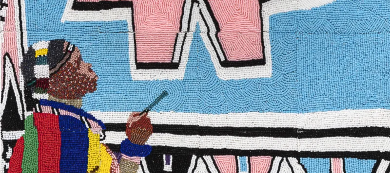 Tiny, colorful beads arranged in patterns to depict Esther Mahlangu painting a large artwork of geometric shapes in light pink and blue, black, white, yellow, and green. She is a dark-skinned adult woman wearing colorfully patterned robes.