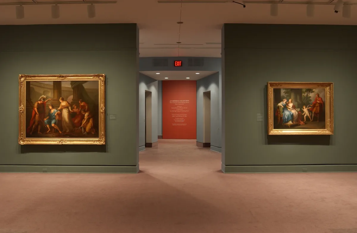 Installation image of an exhibition. Two large oil paintings hang on opposite walls. The walls are painted in sage green. The paintings are framed in golden frames and portray mythical scenes.