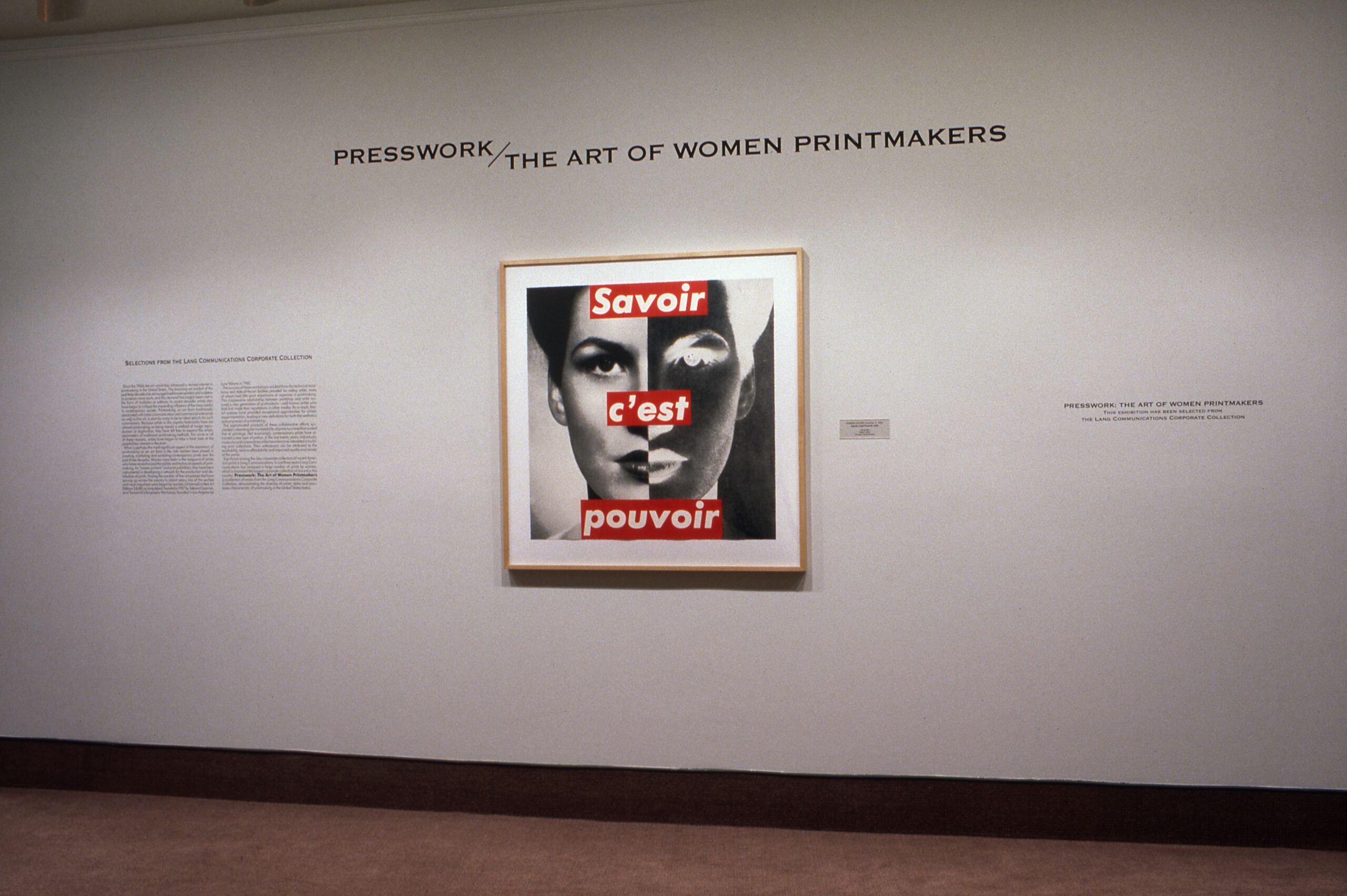 A large photomontage is hanging on a white wall. It's a photograph of a woman's face overlayed with the text 