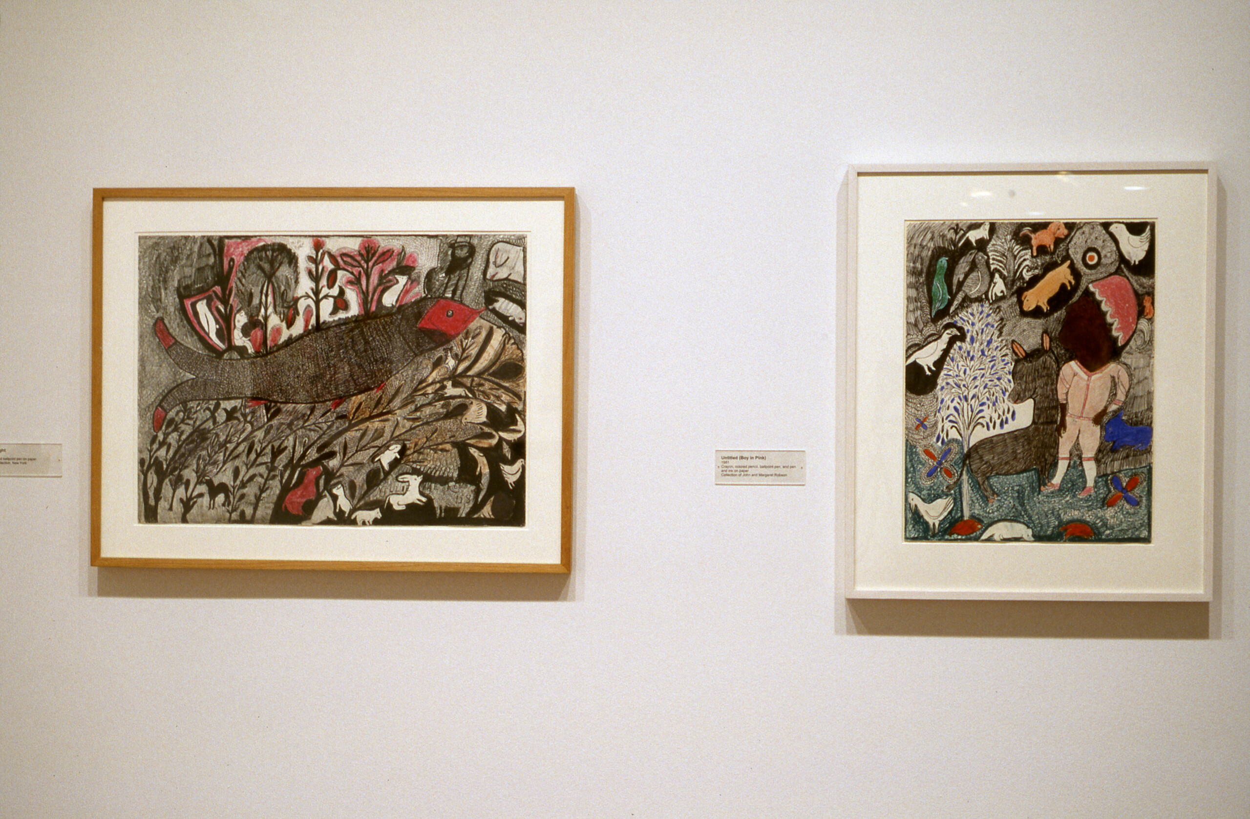 A view of an exhibition space shows two art works hanging on a wall next to each other. The drawings depict colorful animals and people before a gray background.