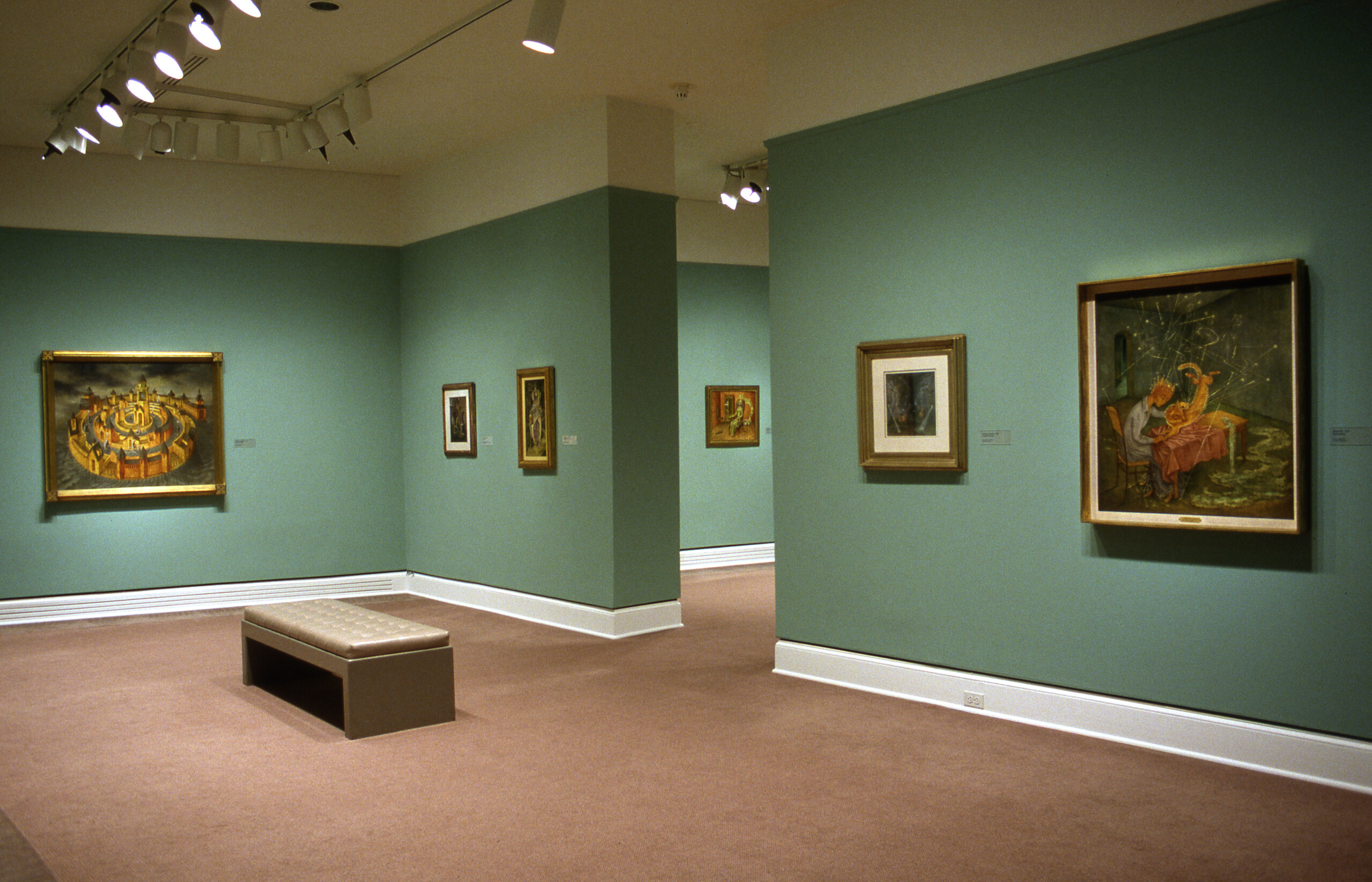 A view of an exhibition space with blue walls. Several paintings are hanging on the walls, depicting surreal scenes.