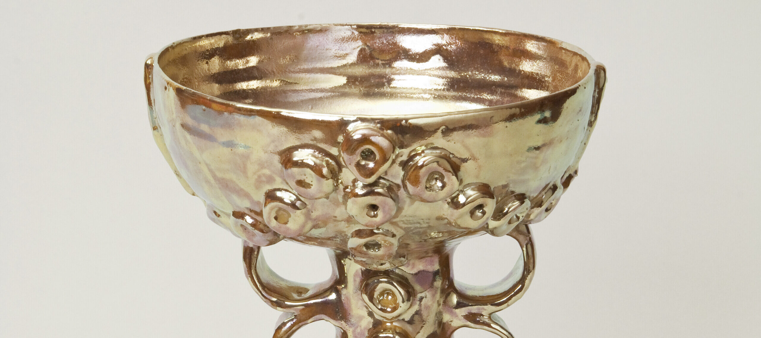 Golden lusterware chalice features a wide bowl above two looped handles on either side of the cone-shaped base. Raised circular decorations adorn the base and the outside of the bowl.