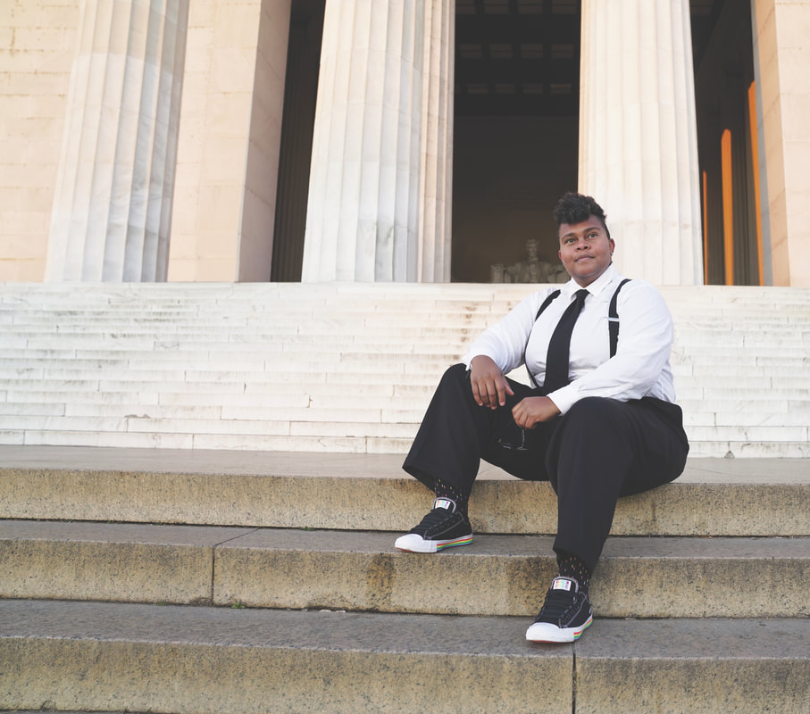 A person with medium skin tone sits on the stairs of the Lincoln Memorial, a white stone building with fluted columns.