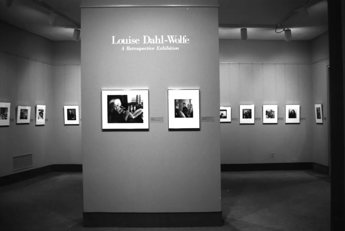 A view of a gallery space. The black-and-white photograph shows several photographs hanging on a white wall. Above the photographs, it says in big letters: "Louise Dahl-Wolfe: A Retrospective Exhibition."