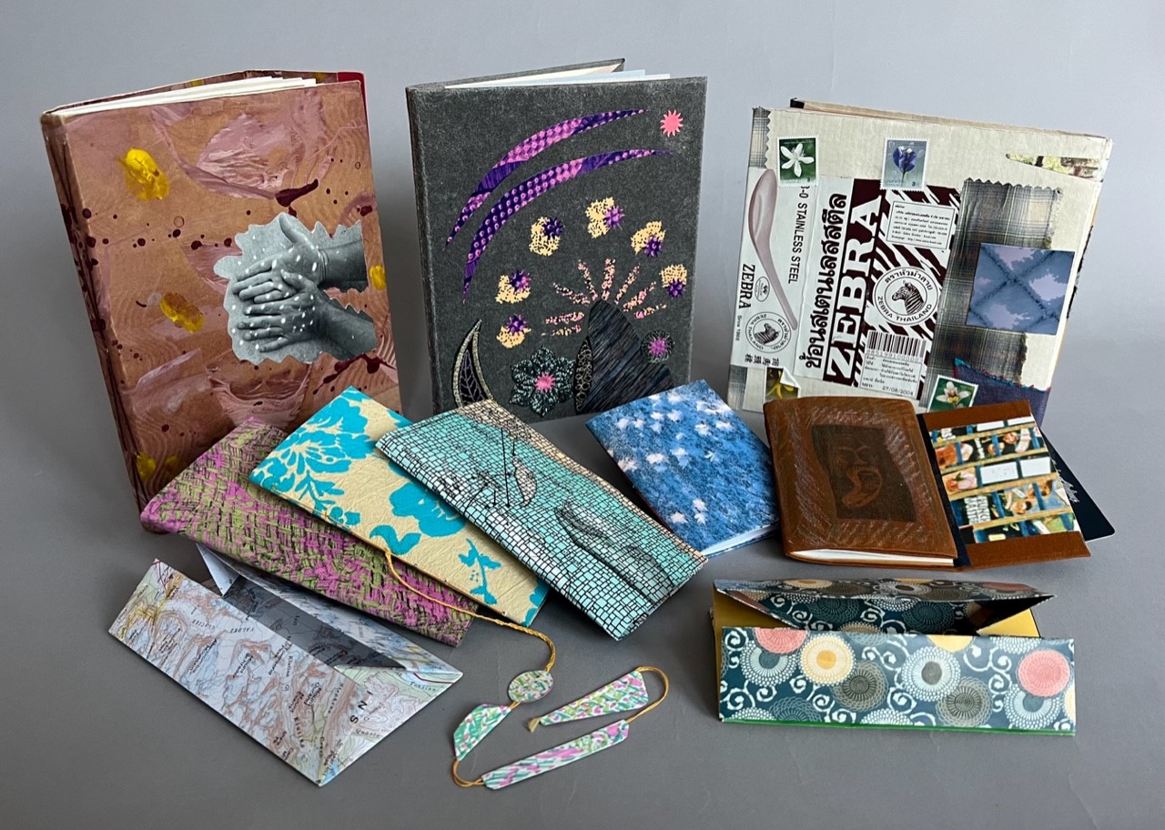 A photograph of a collection of brightly colored travel journals with collaged covers.