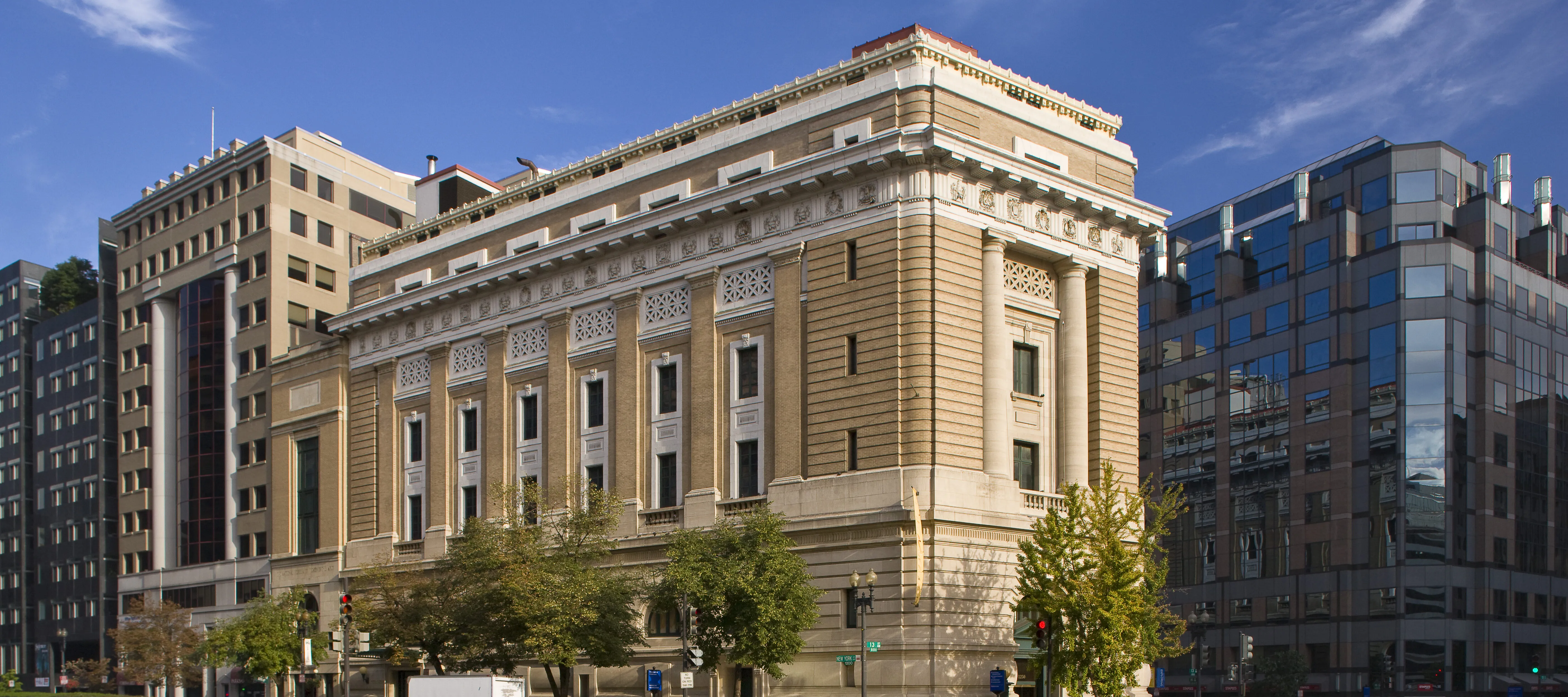 View of the museum from outside showing the Neoclassical building from one corner. The building is a tan-colored stone with an arched doorway, long vertical windows, and detailed molding around the roof.