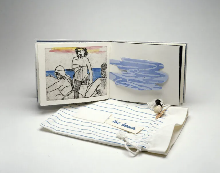 An open book is in the background and its cover is in the foreground. The left book page features a print of three figures on a beach and the right book page has a blue, amorphous shape with wavy lines. The book cover is a drawstring bag made of striped blue and white fabric. On top, it has a pocket that holds a card which reads “the beach” and is ornamented with seashells.