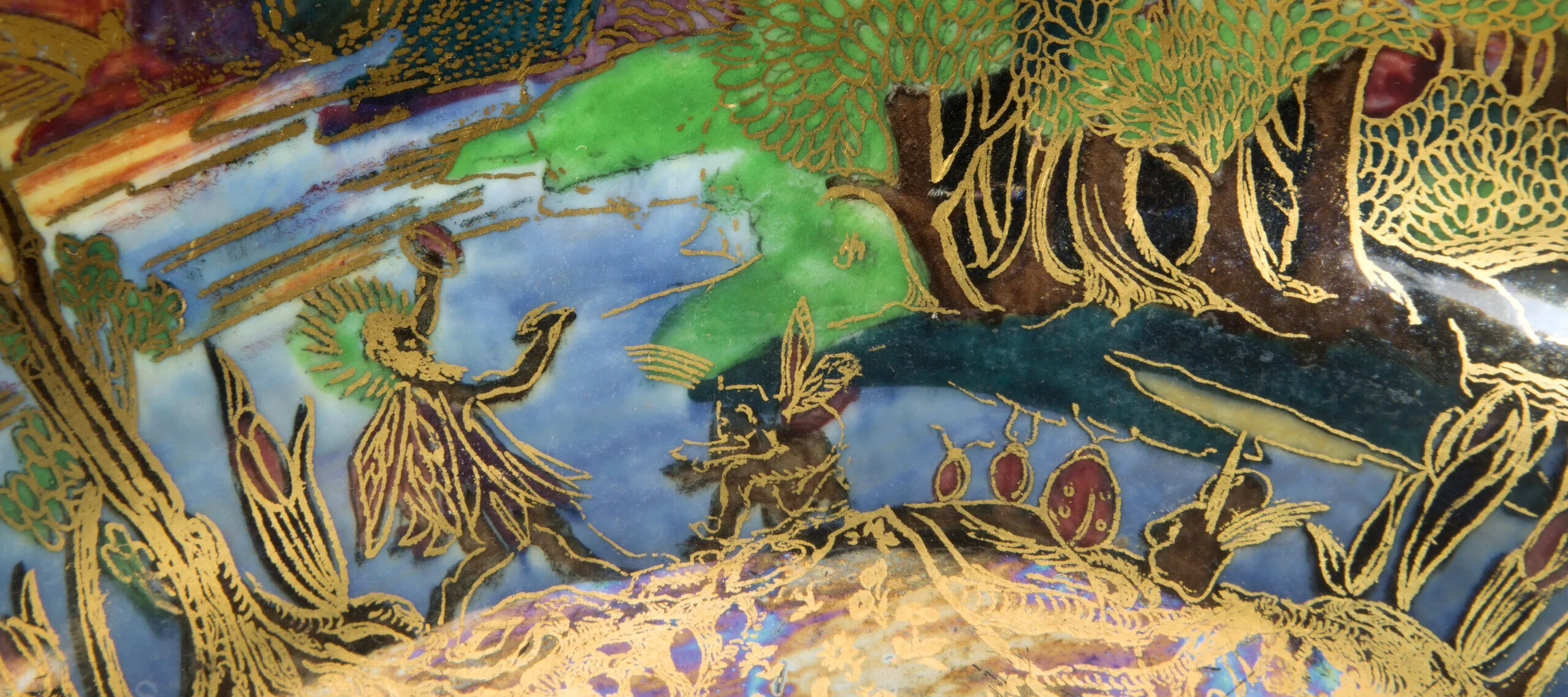 Detail image of a ceramic punchbowl painted with blue, green, red, and purple tones. The details of a mythological scene are painted in gold on top of the swaths of color.