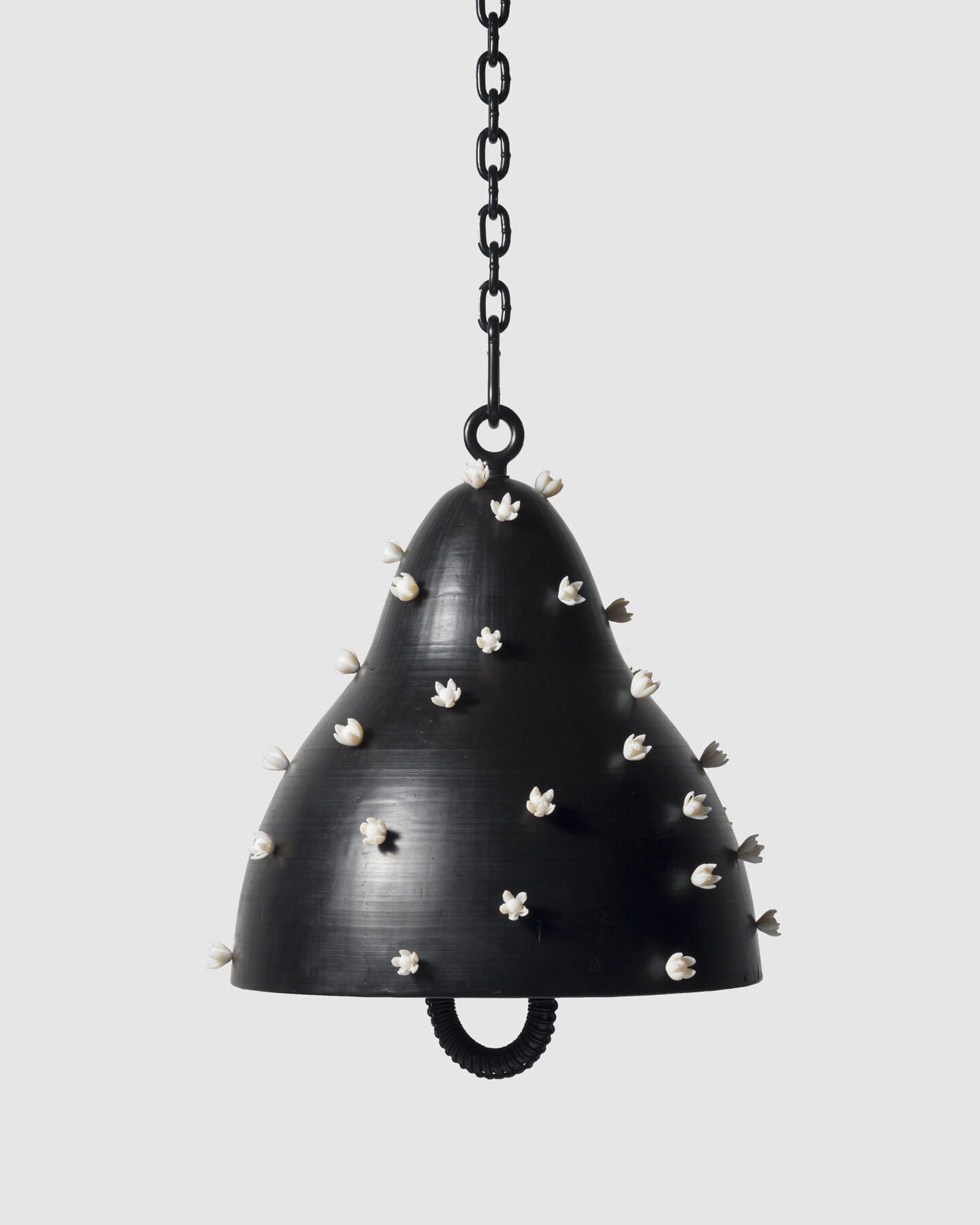 A black bell covered in three-dimensional white flowers with a black clapper, hanging from a black chain.