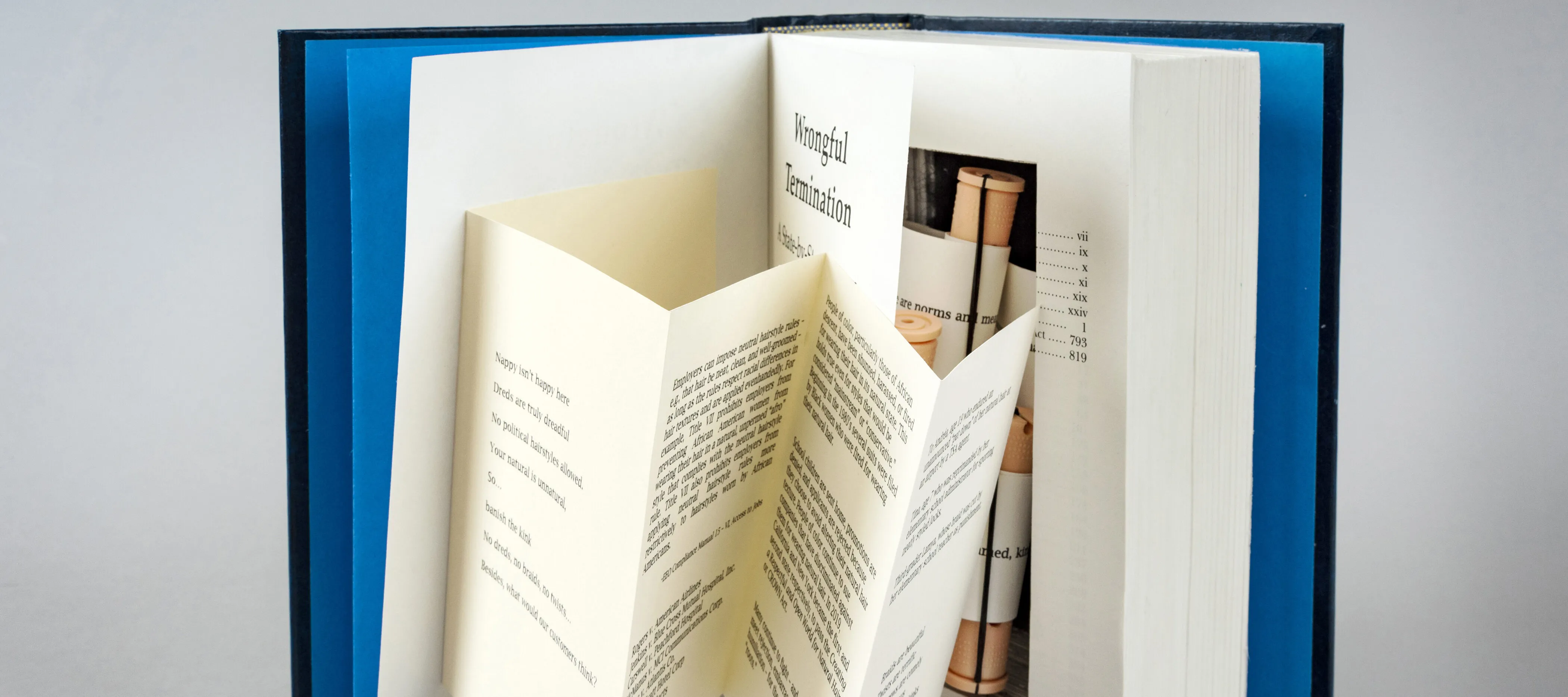 A photograph of an altered book opened to reveal an accordion page extending from the title page on the left and a secret compartment inside the body of the book on the right.