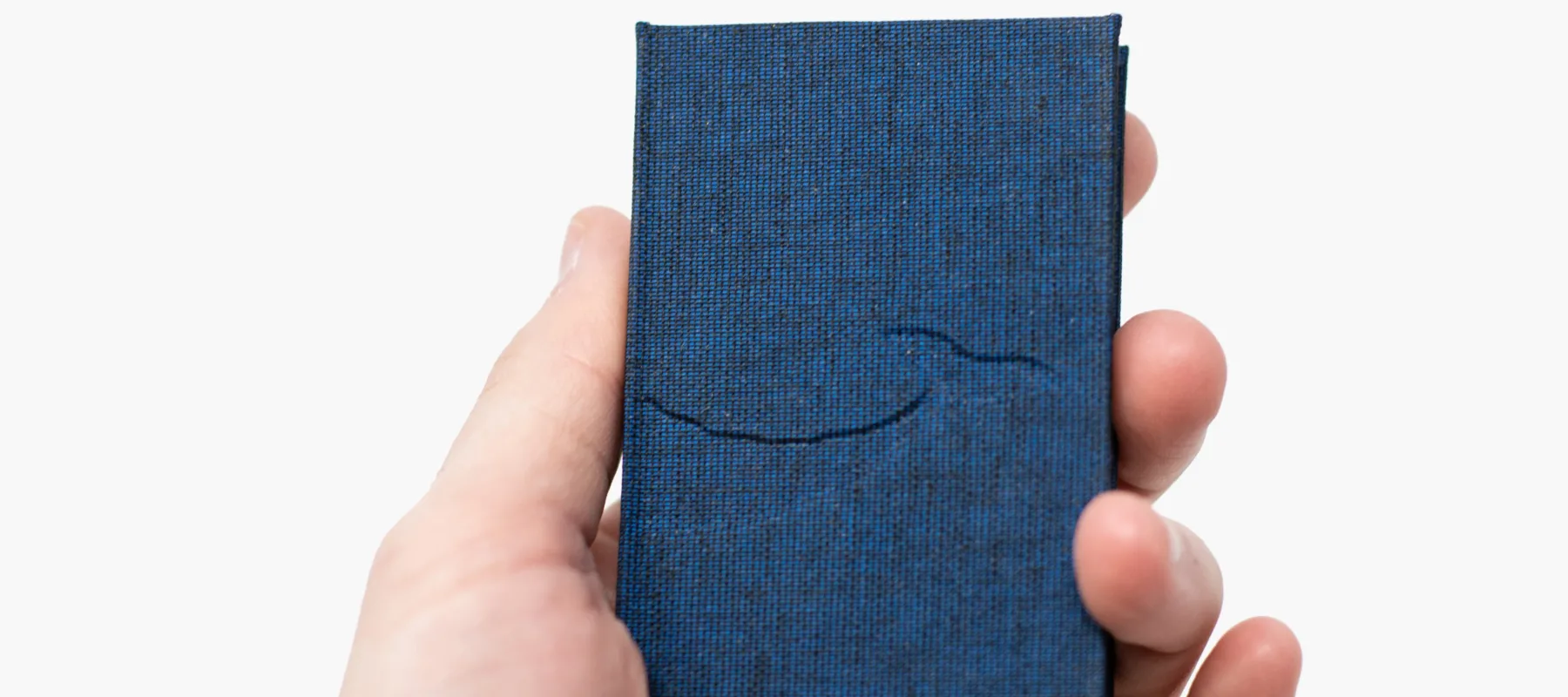 A close-up photograph of a light-skinned hand holding a small blue book with an embossed cover.