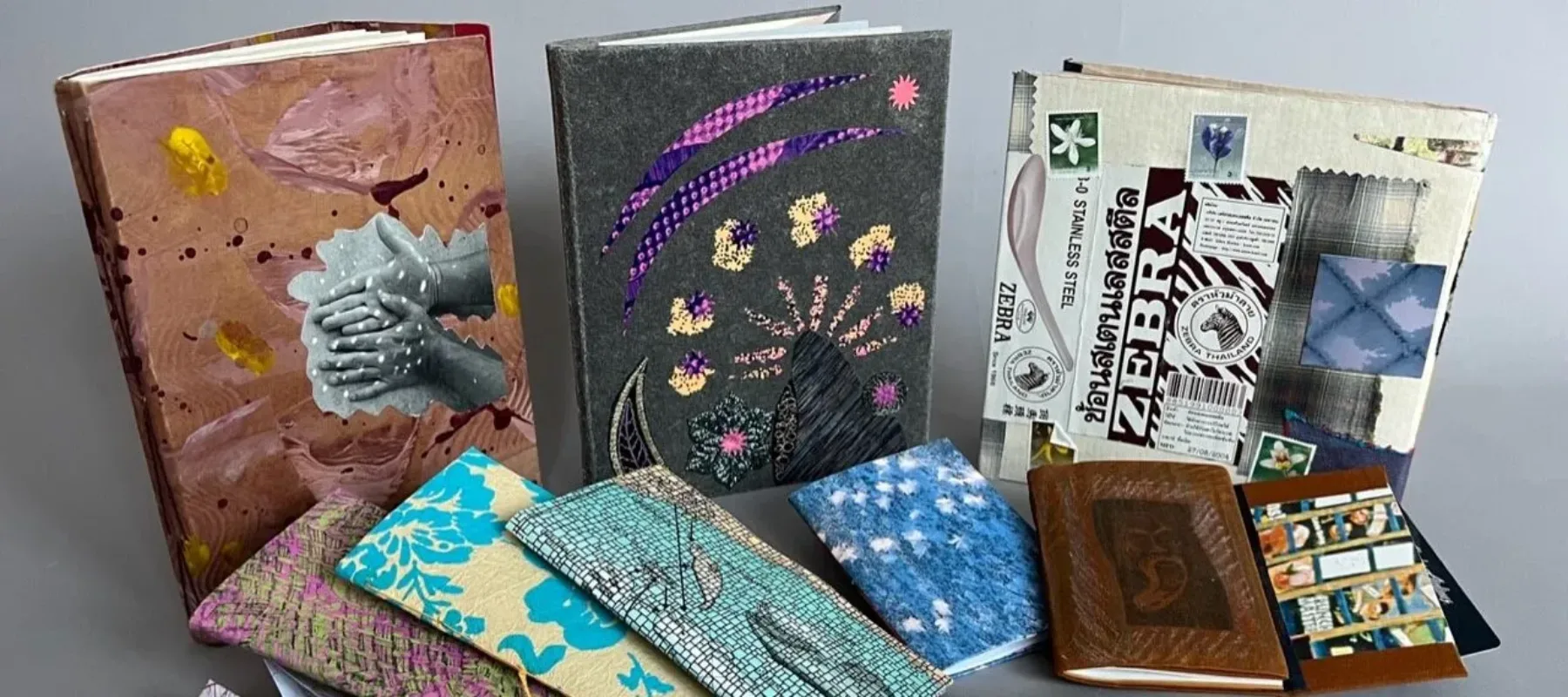 A photograph of a collection of brightly colored travel journals with collaged covers.