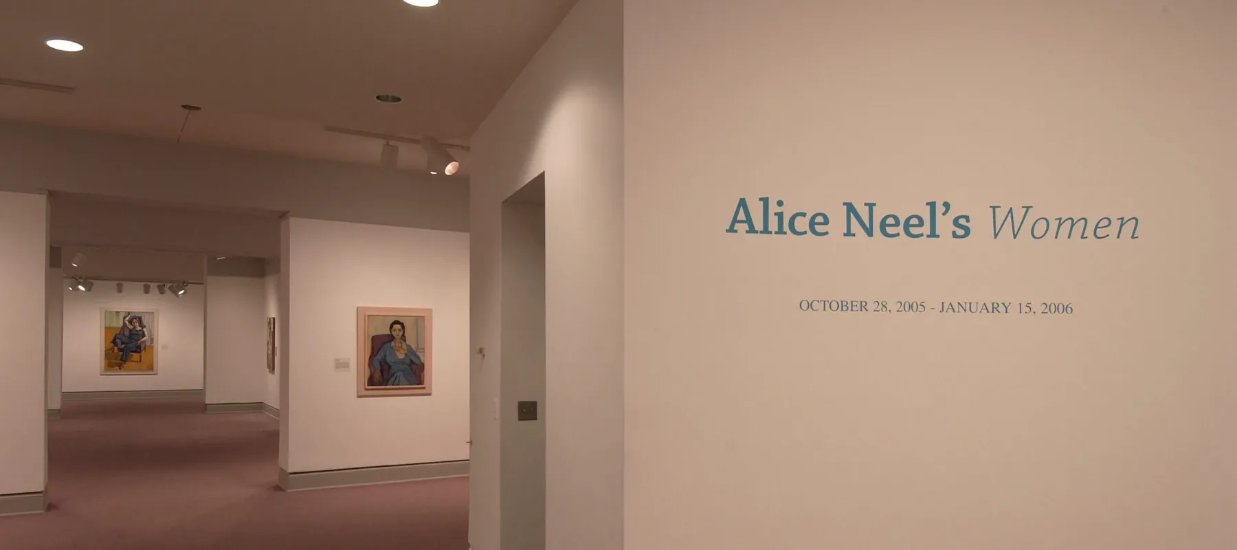 An installation view of a gallery space shows several paintings hanging on a white wall. On another wall, it says in big blue letters: "Alice Neel's Women".