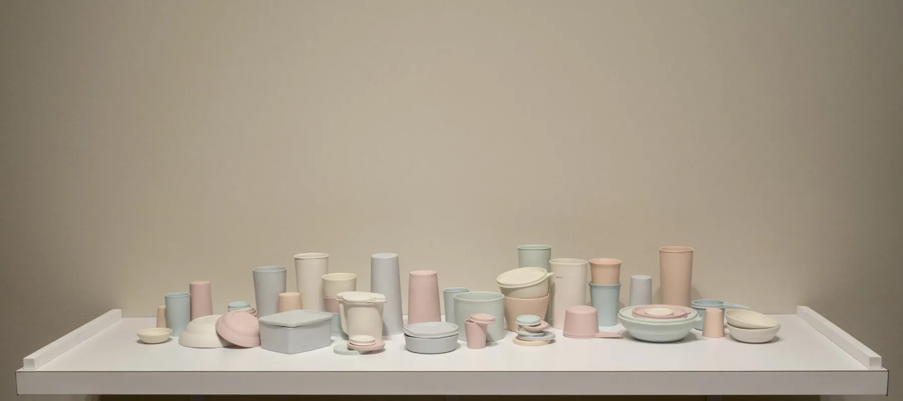 A collection of pastel-colored porcelain cups, bowls, containers, and lids that resemble plastic food containers. Some are stacked within and on top of each other. Some containers have lids firmly shut while on others the lids teeter off the edge of container rims.