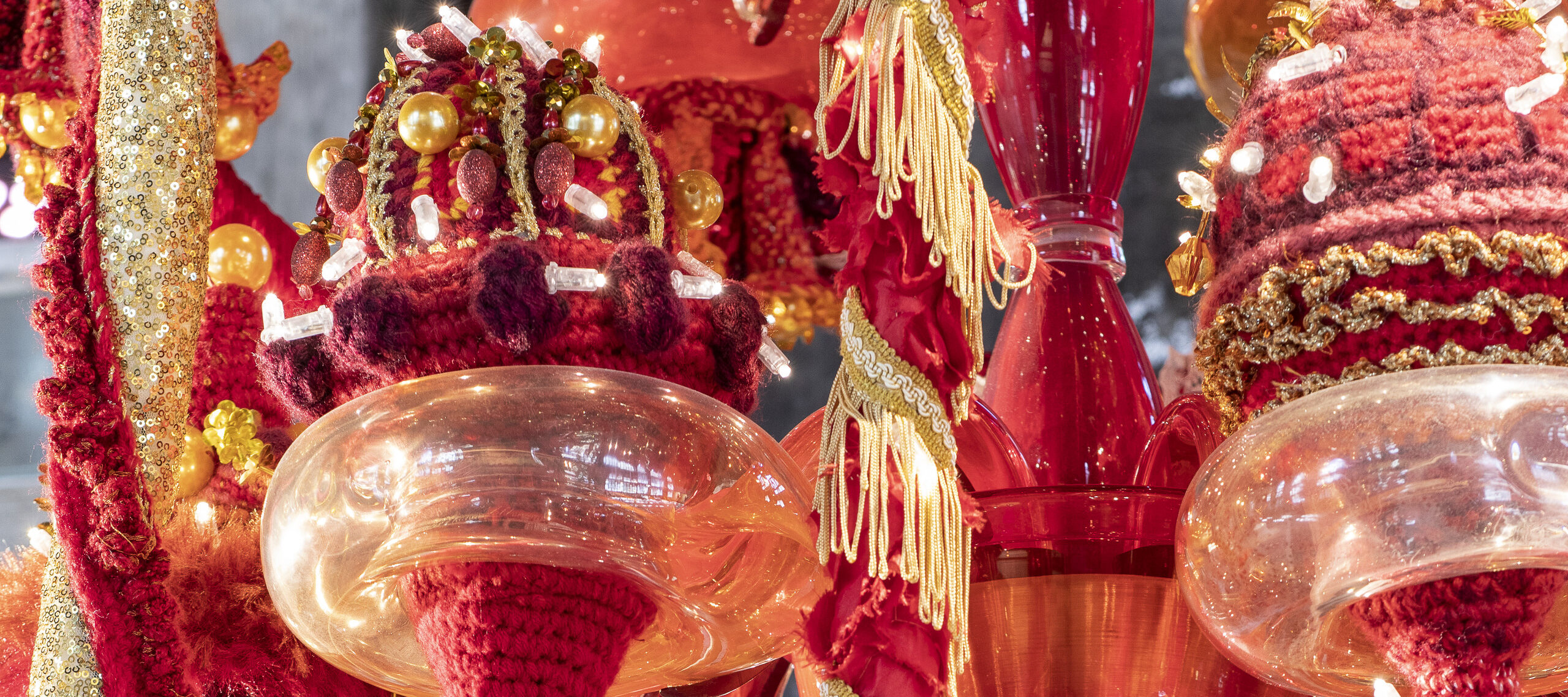 A color image of a detail of a chandelier made of red, orange, and yellow Murano glass, wool yarn, polyester fabrics, and LED lighting.