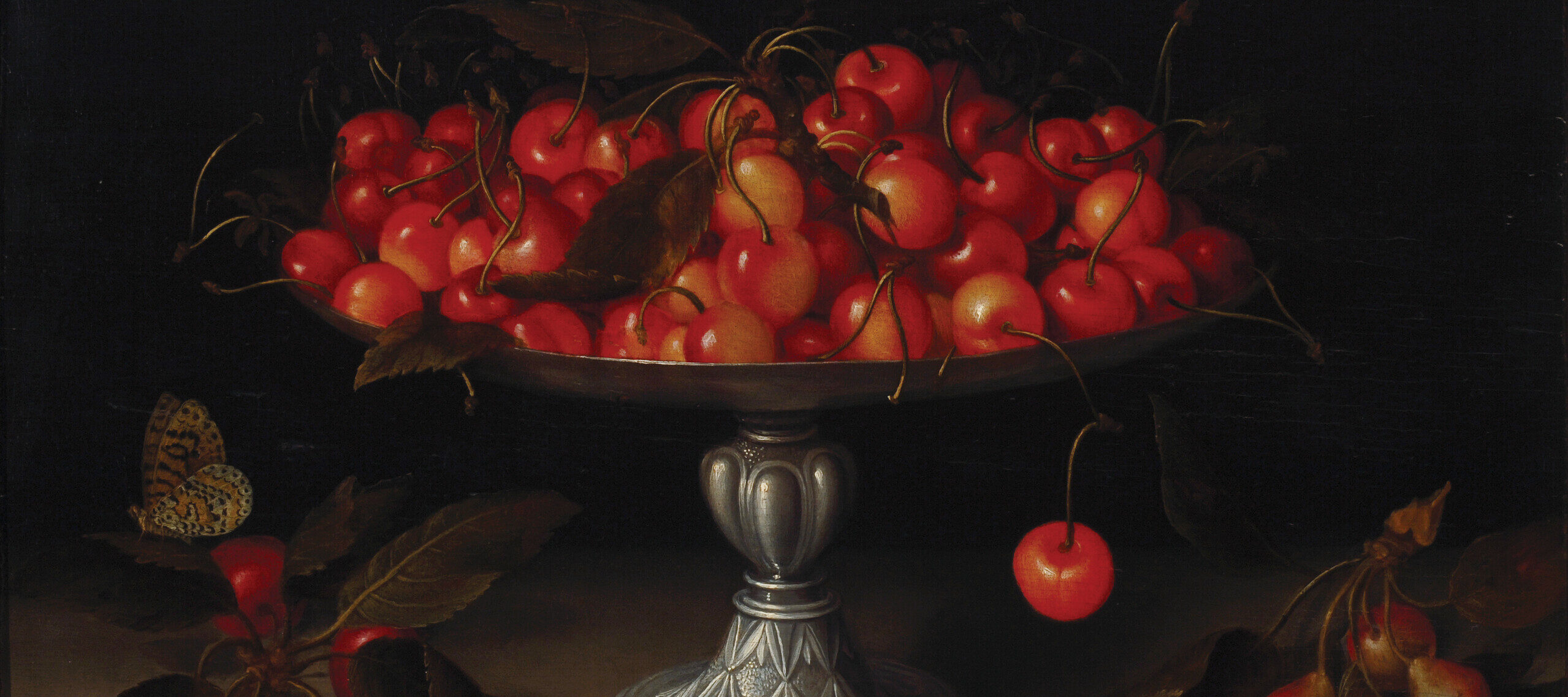An opulent, footed silver bowl overflows with ripe cherries in front of a dramatic dark background. Additional fruits lie on the table below the bowl, and a butterfly flutters to one side.