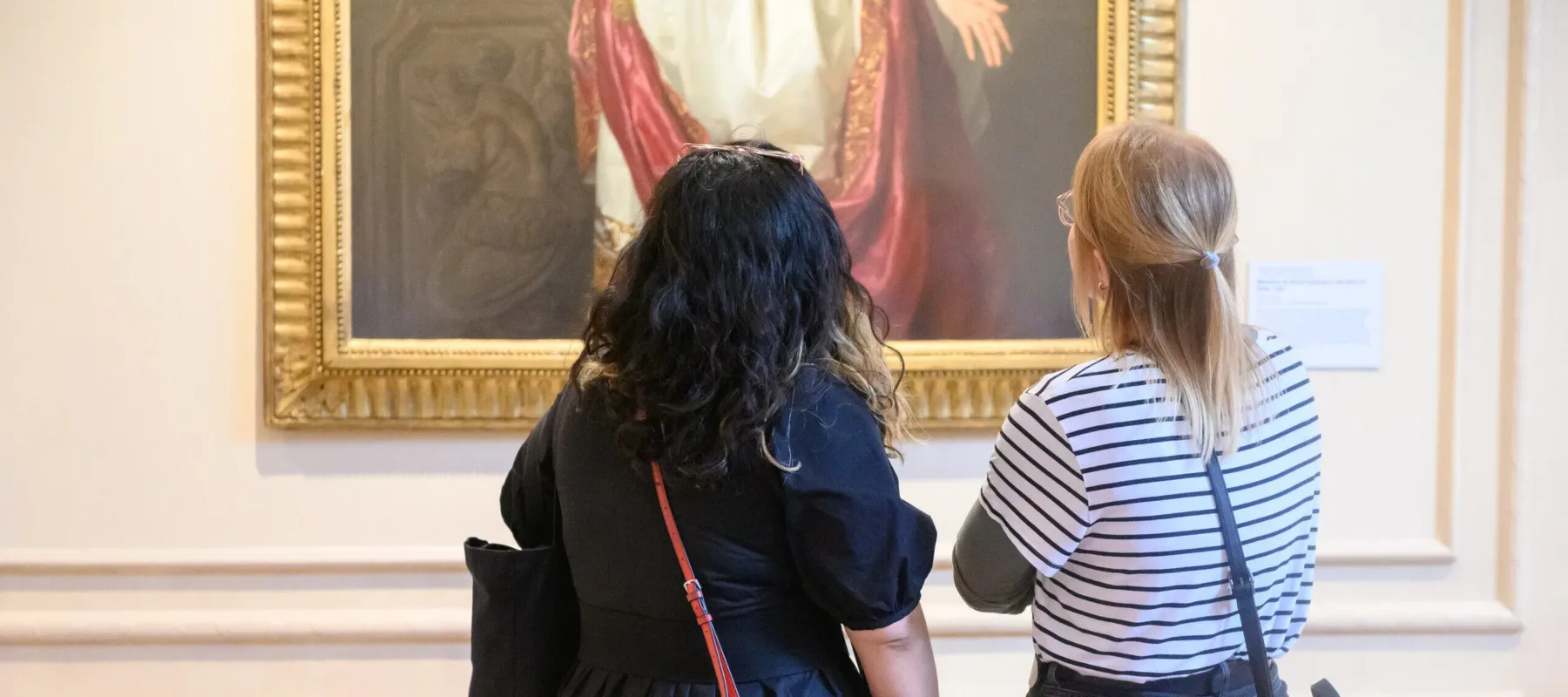 Two individuals look closely at a painting in museum gallery.