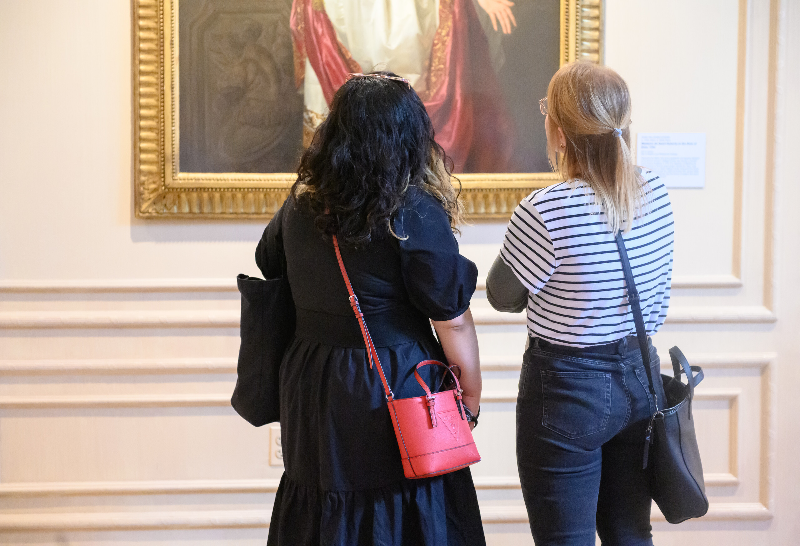 Two individuals look closely at a painting in museum gallery.