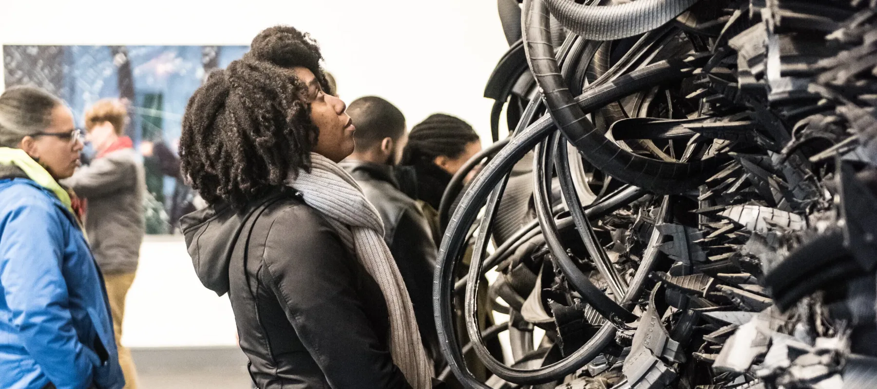 A woman looks closely at a large sculpture made of tires in a museum gallery.