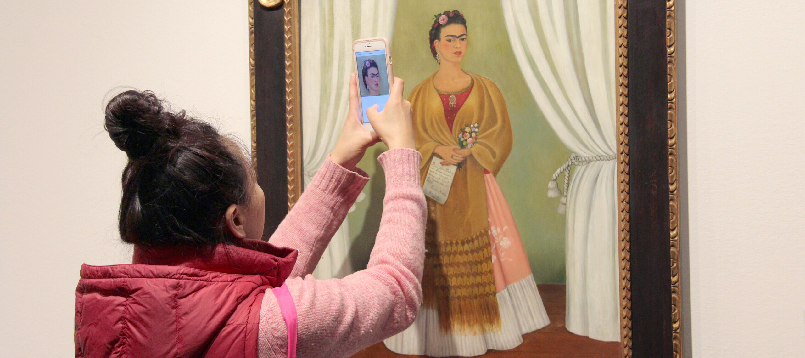 An individual takes a closeup photo of a Friday Kahlo portrait in the museum's galleries.