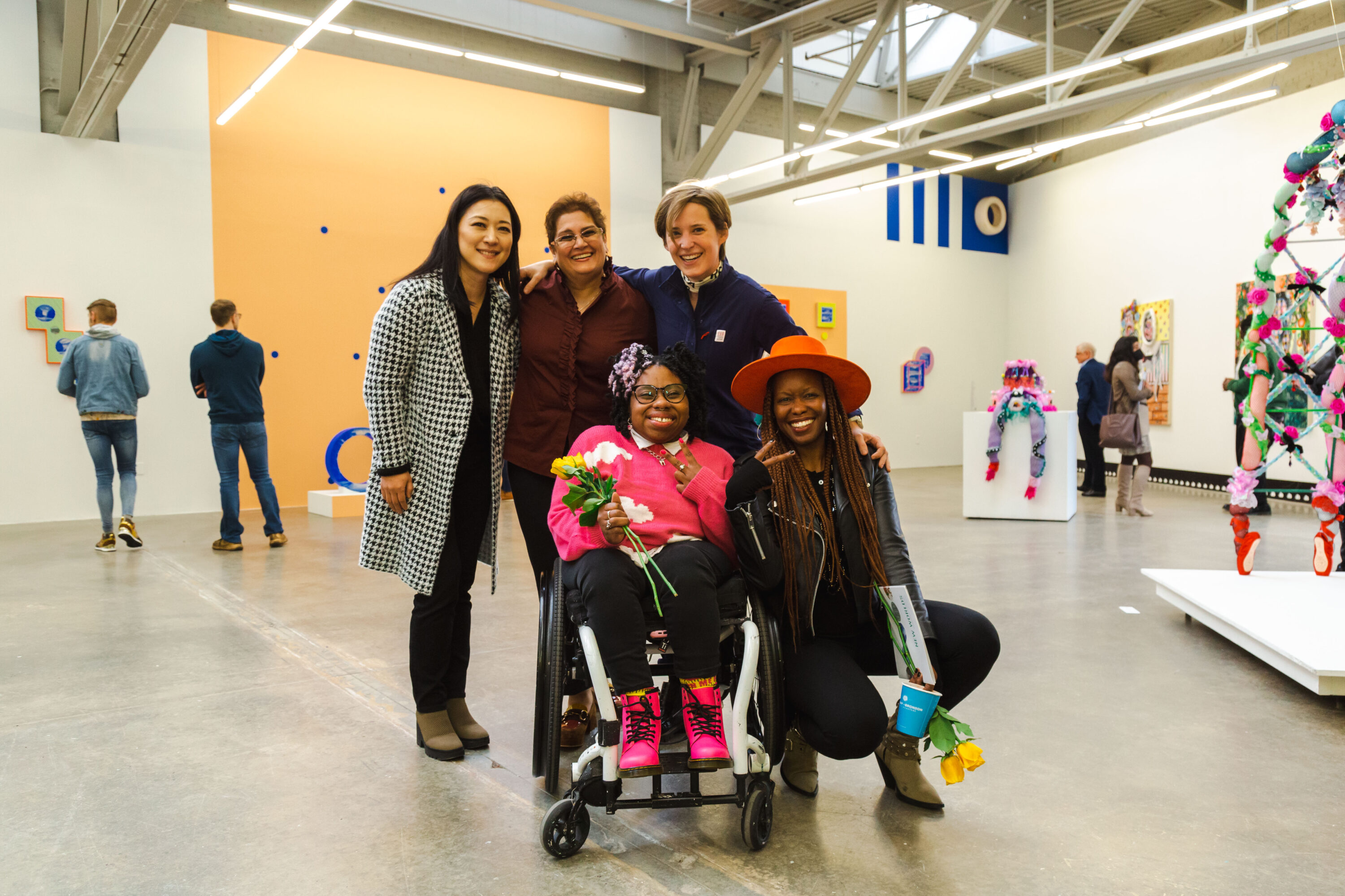 A group of women pose for a photograph in a gallery space filled with colorful sculptures and two dimensional works.