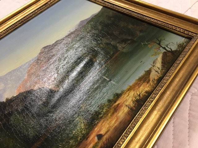 An oil painting of a serene landscape scene is photographed from an angle to show a large lump in the middle of the canvas where the work is separating from its canvas lining.