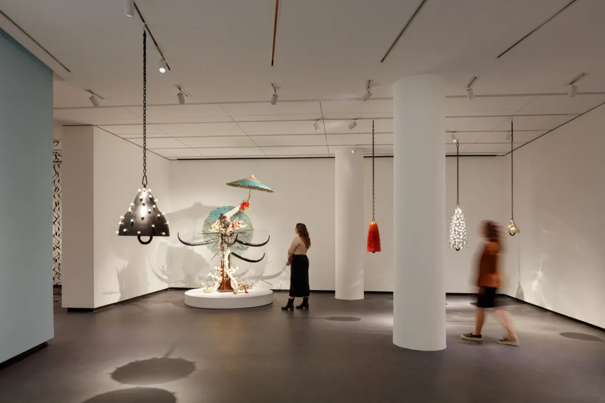 A modern museum gallery is photographed at a wide angle. Visitors observe large sculptures, several of which hang from the ceiling.