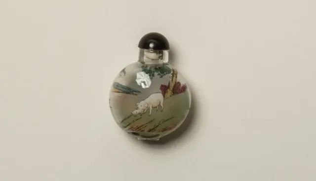 A woman wearing an elaborate hairstyle and earrings is seen in profile against a cream background and outlines of butterflies. A decorative glass bottle and two miniature ceramic sculptures of male figures are attached to the surface of the print.