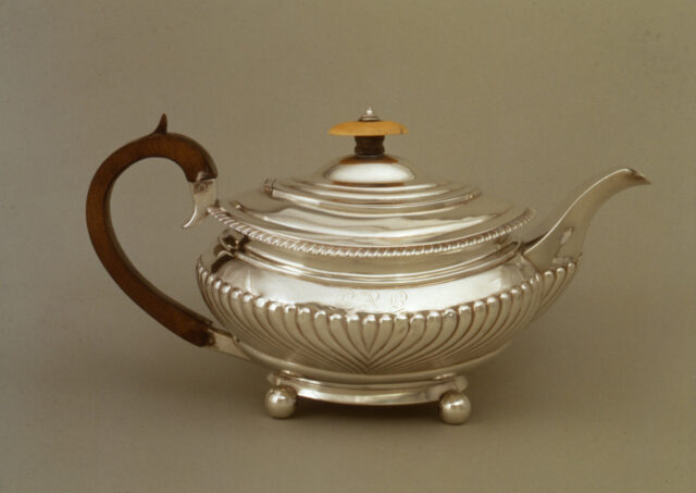 A squat silver teapot with a fluted body, wooden handle and wood and ivory or bone finial.