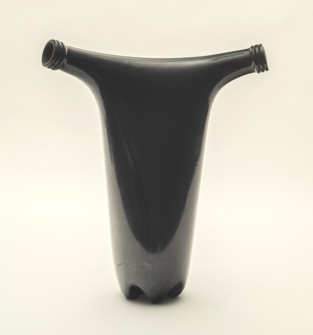 A black sculpture made from two bottles merged together. The shape of the double-spouted vase is reminiscent of a uterus. The shiny black finish gives it a precious look, while the plastic bottle shape juxtaposes this notion of a precious object.
