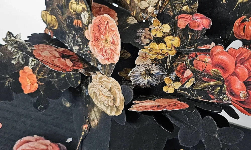 An artist's book, opened to reveal a pop-up of many colorful flowers in a vase. The pages are dark with black writing.