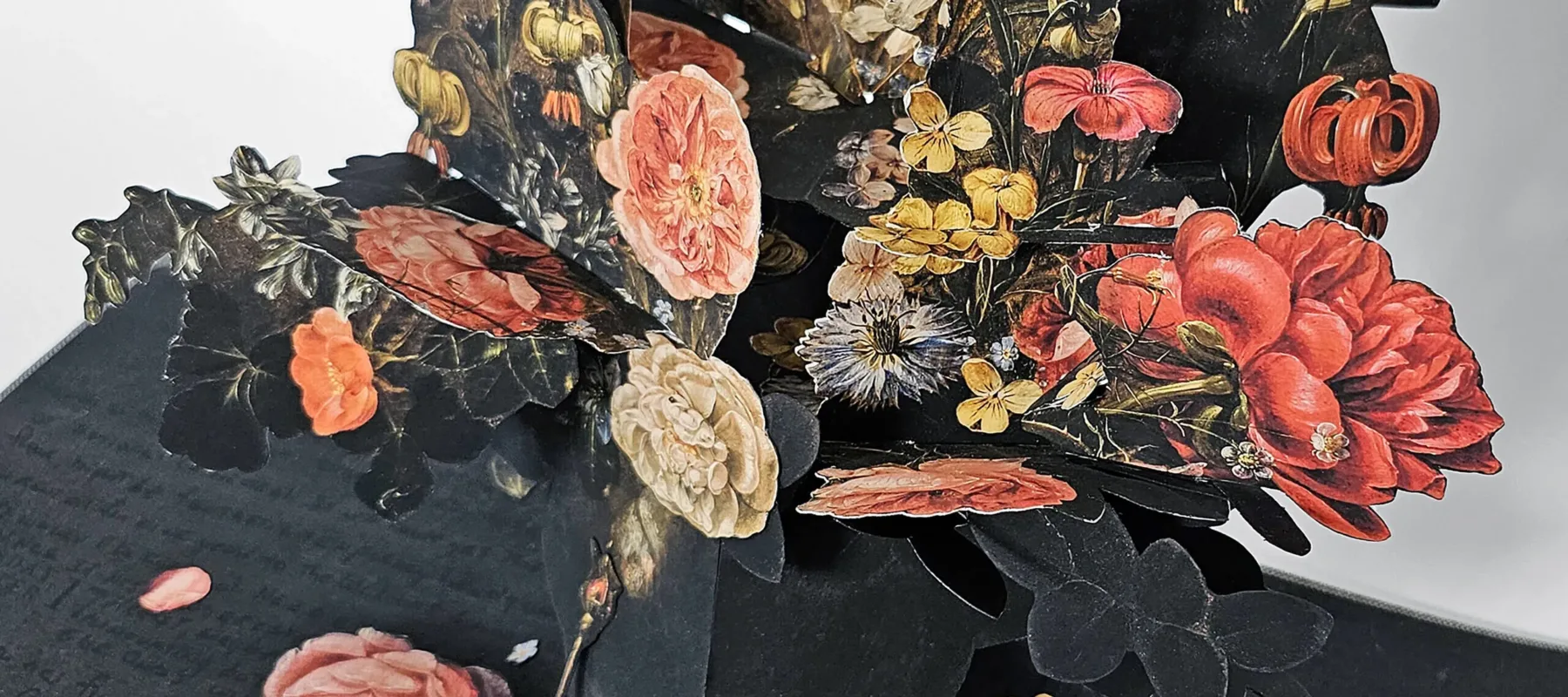 An artist's book, opened to reveal a pop-up of many colorful flowers in a vase. The pages are dark with black writing.