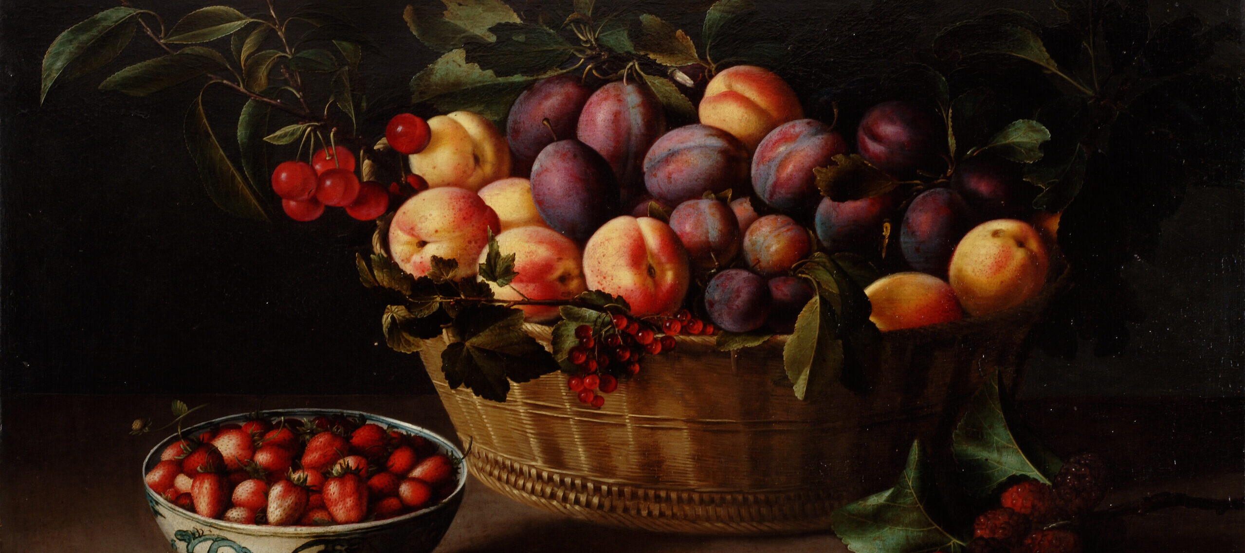 A brightly lit basket of peaches and plums on a ledge against a dark background. To the left of the basket is a blue and white porcelain bowl filled with strawberries. A whole fig sits next to it. In front of the basket is half of a fig and to the right a branch with leaves and red berries.
