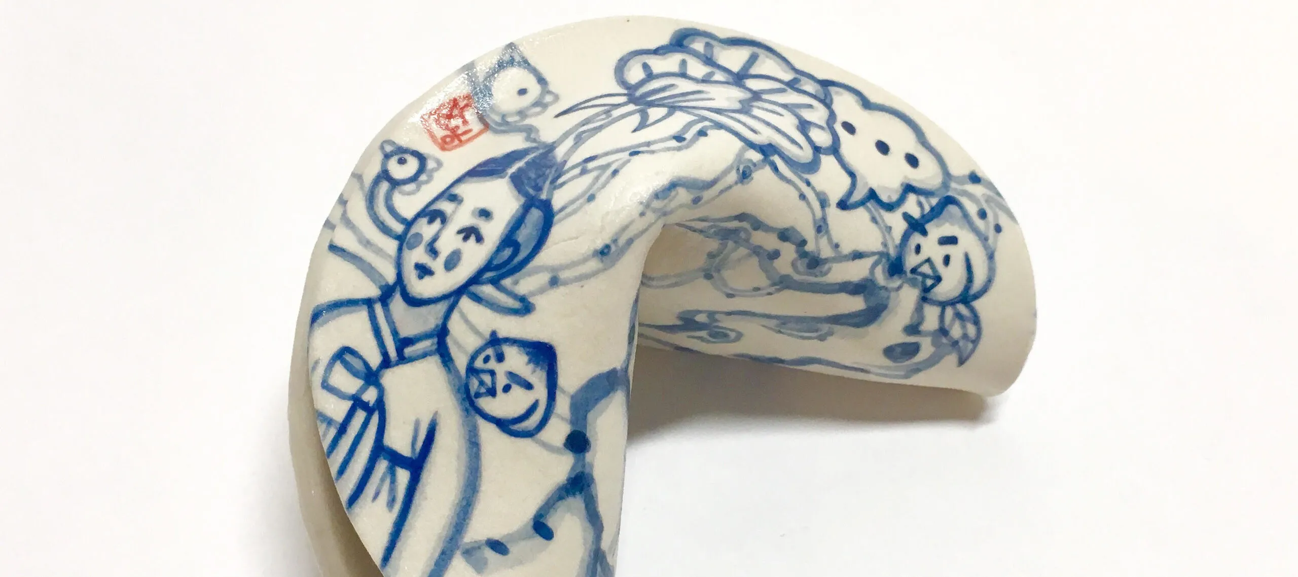 A blue and white painted porcelain fortune cookie depicting a woman in a hanbok standing in a garden of tall trees dotted with large peaches with faces and beaks on them. On the cookie’s edge is a red stamp with the artist’s name.