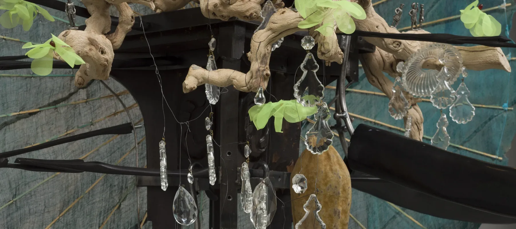 A detail image of a sculpture made of blue parasols, a black wooden rhino figurine, white cowry shells, a red doll's head, and other natural materials.