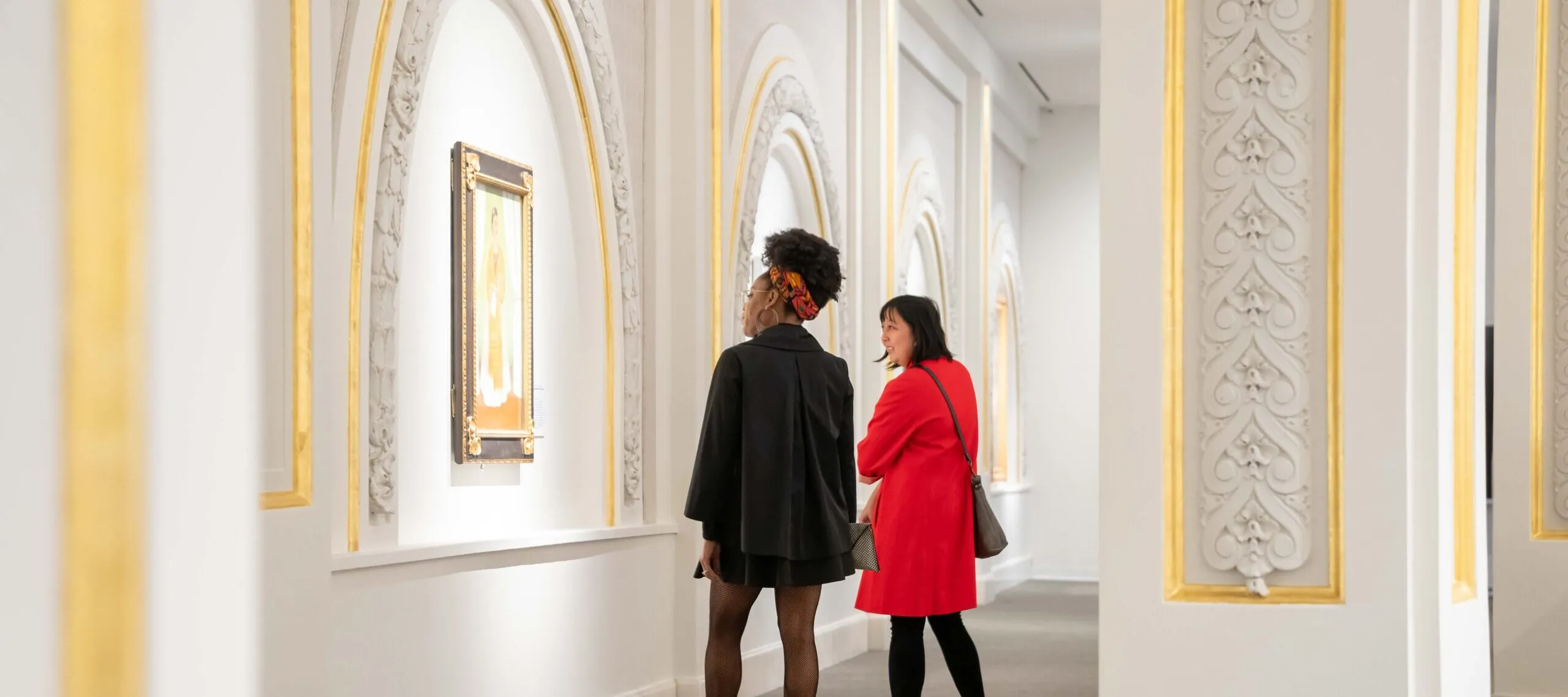 Two museum visitors observe artworks in a modern gallery.