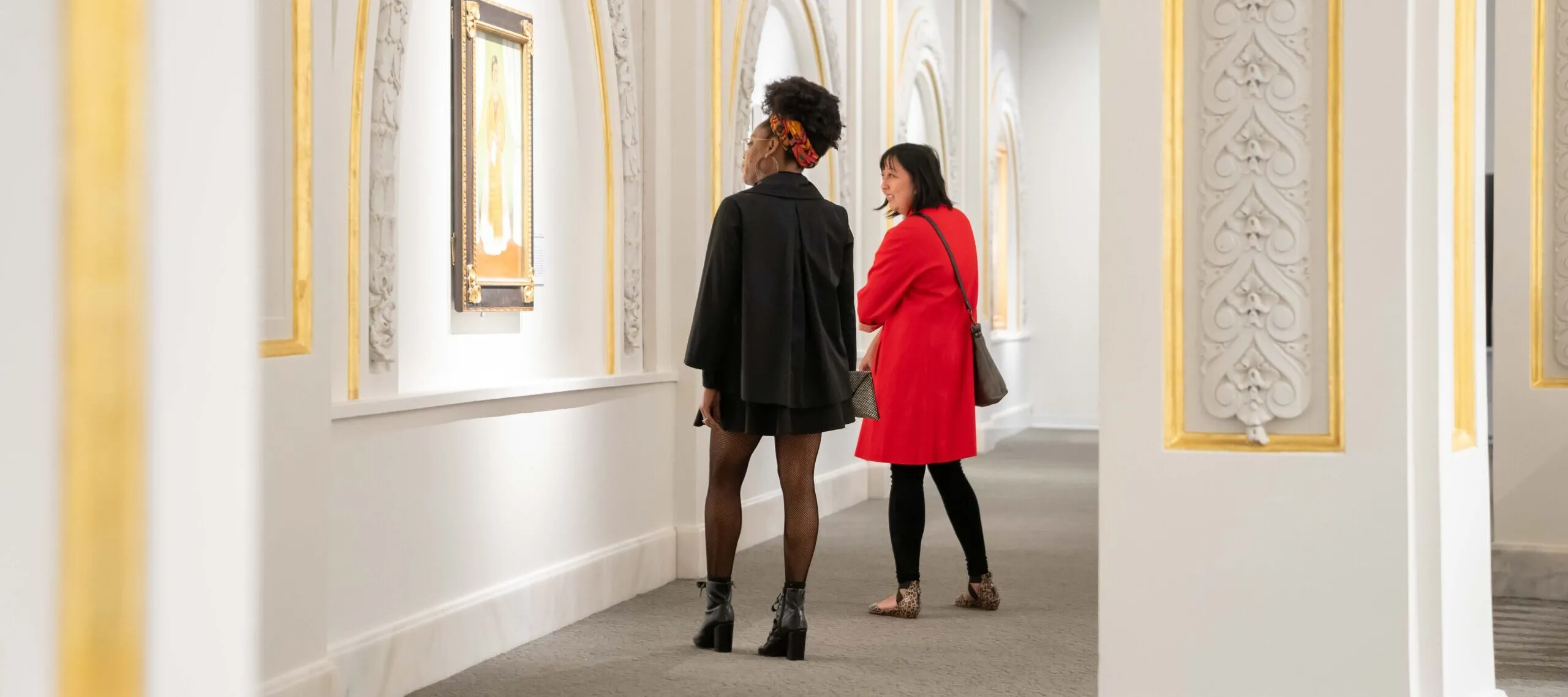 Two museum visitors observe artworks in a modern gallery.