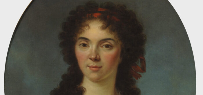 Oval portrait of a young woman with light skin gazes out at the viewer with her dark tousled curls framing her face and shoulders.