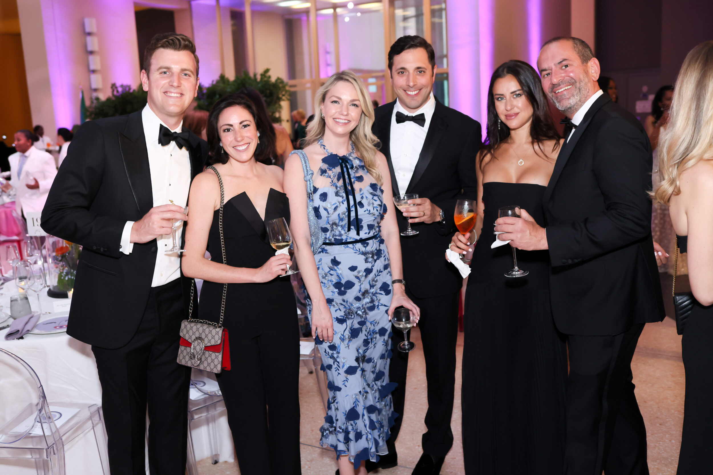 A small group of light-skinned men and women pose for a photo at a black-tie event.