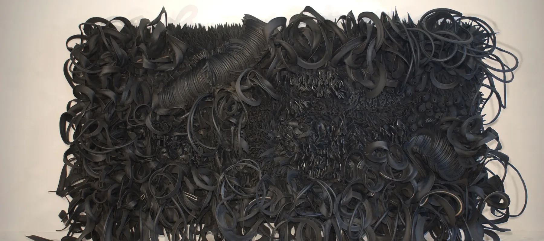 The wall-sized, horizontal sculpture consists of black rubber tires and tubing that has been sliced, stripped, woven, looped, twisted and otherwise manipulated into an expressive and abstract high-relief tableau.