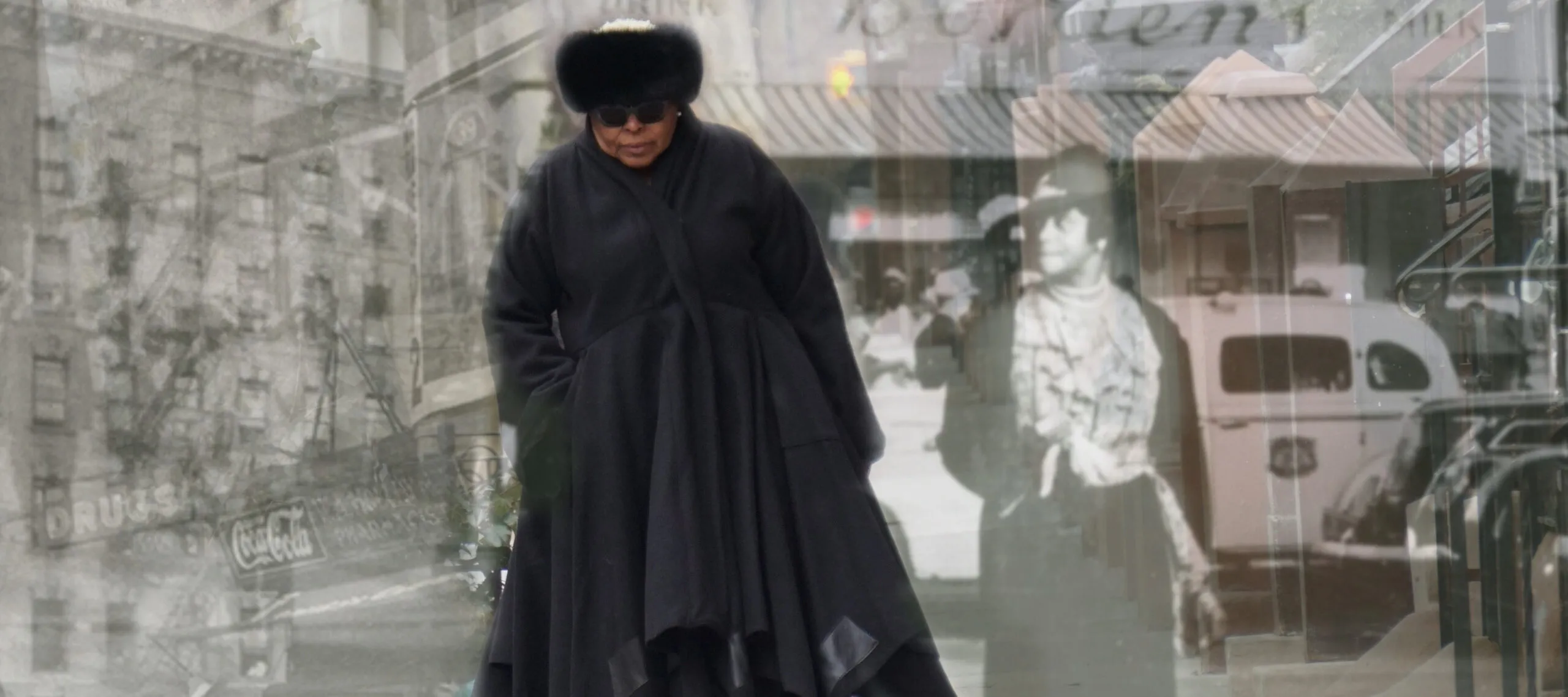 A medium-dark skinned adult woman wearing all black—a fur hat, sunglasses, boots, and a long, voluminous coat—walks on a sidewalk toward the viewer. Black and white images of people and buildings in Harlem from the early 20th century are layered over the woman.